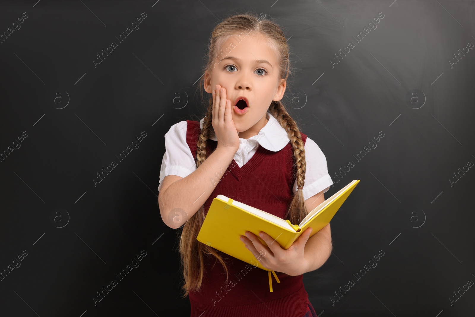 Photo of Emotional schoolgirl with open book near blackboard