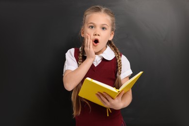 Emotional schoolgirl with open book near blackboard