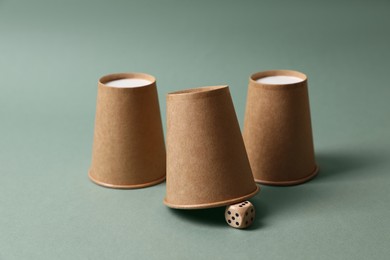 Three paper cups and dice on pale olive background. Thimblerig game