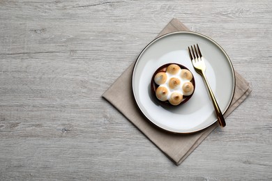 Delicious salted caramel chocolate tart with meringue served on light beige wooden table, top view. Space for text