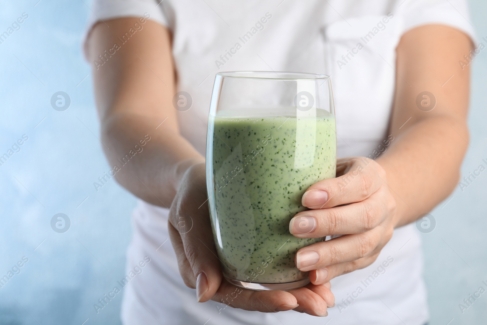 Photo of Woman holding green buckwheat smoothie on light blue background, closeup