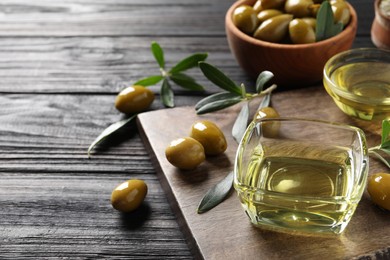 Photo of Glass bowls of oil, ripe olives and green leaves on black wooden table. Space for text