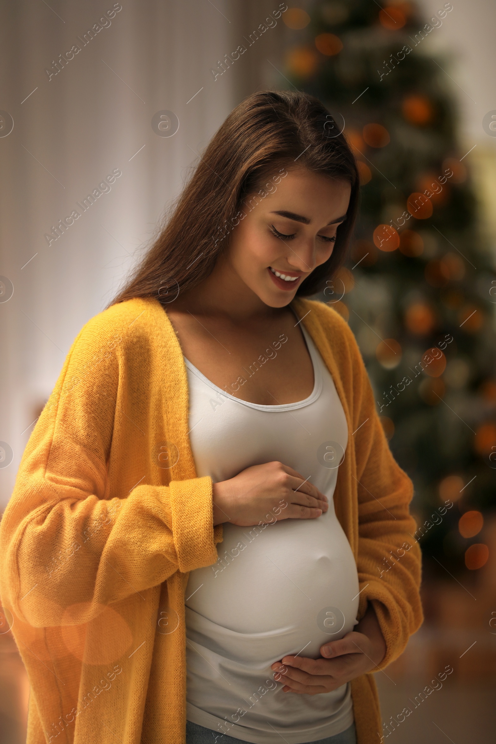 Photo of Happy pregnant woman and Christmas tree on background. Expecting baby