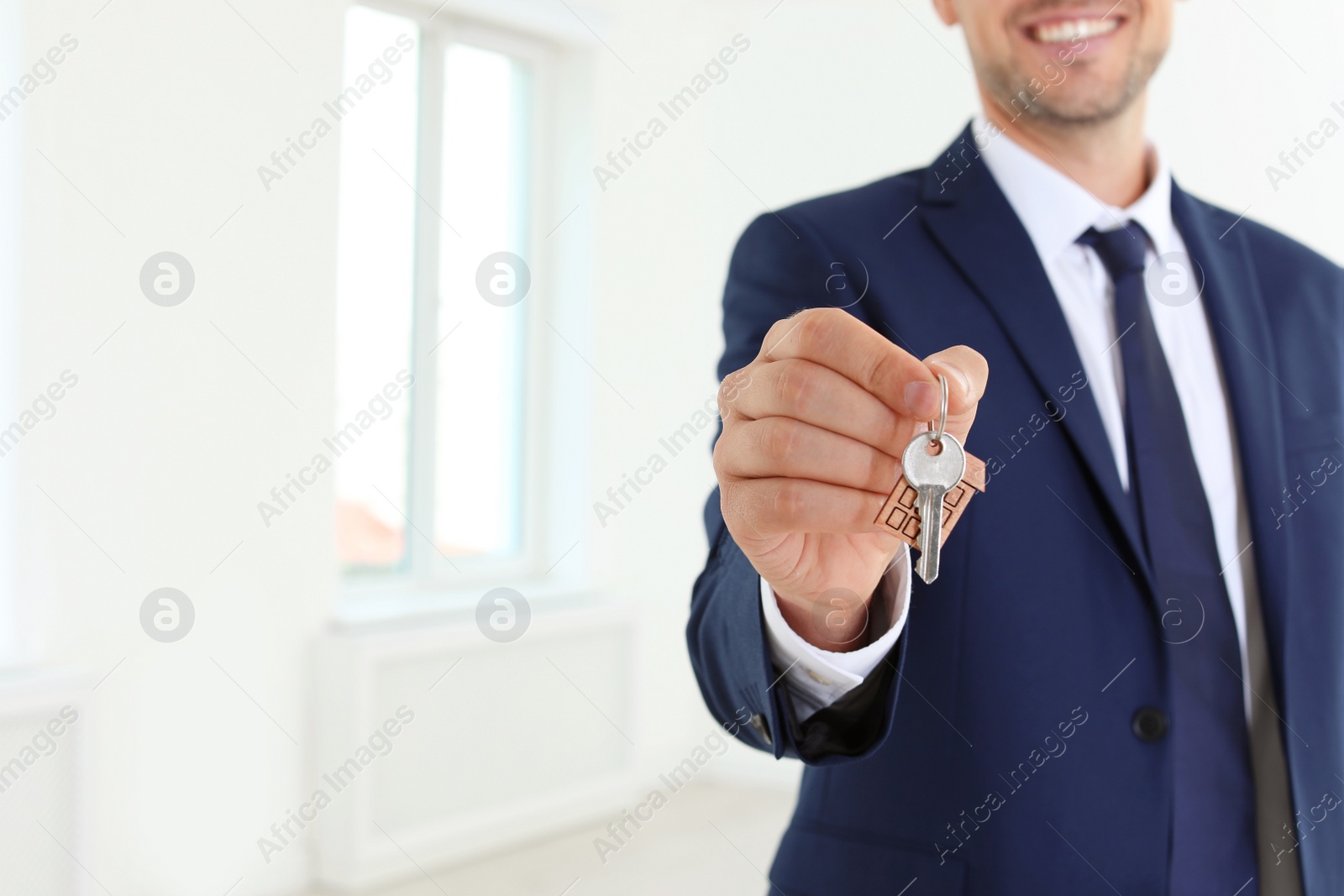 Photo of Real estate agent holding key on blurred background, closeup