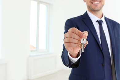 Real estate agent holding key on blurred background, closeup
