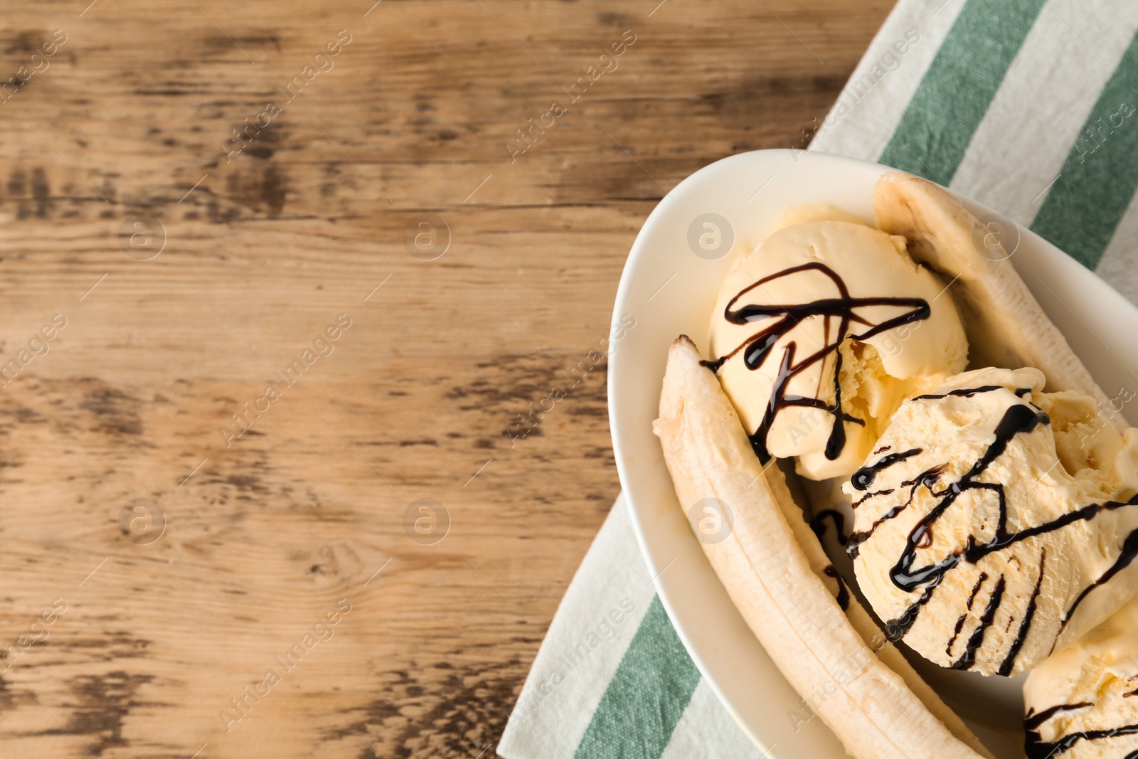 Photo of Delicious banana split ice cream with chocolate topping on wooden table, top view. Space for text