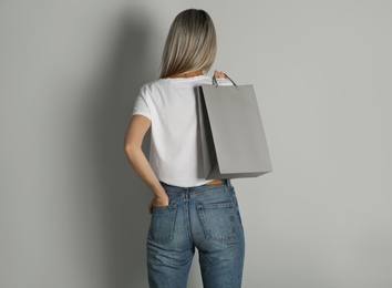 Photo of Woman with paper shopping bag on light grey background, back view