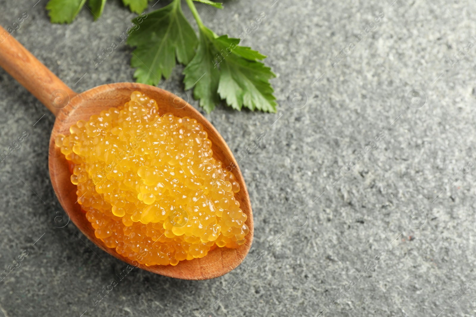 Photo of Fresh pike caviar in spoon and parsley on grey table, top view. Space for text