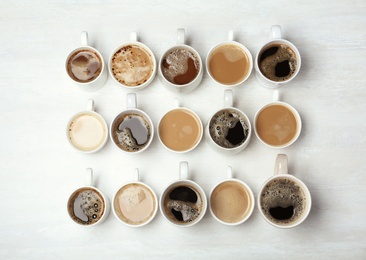 Photo of Many cups with tasty aromatic coffee on wooden table, flat lay
