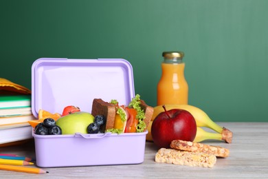 Photo of Lunch box with healthy food and different stationery on light wooden table near green chalkboard