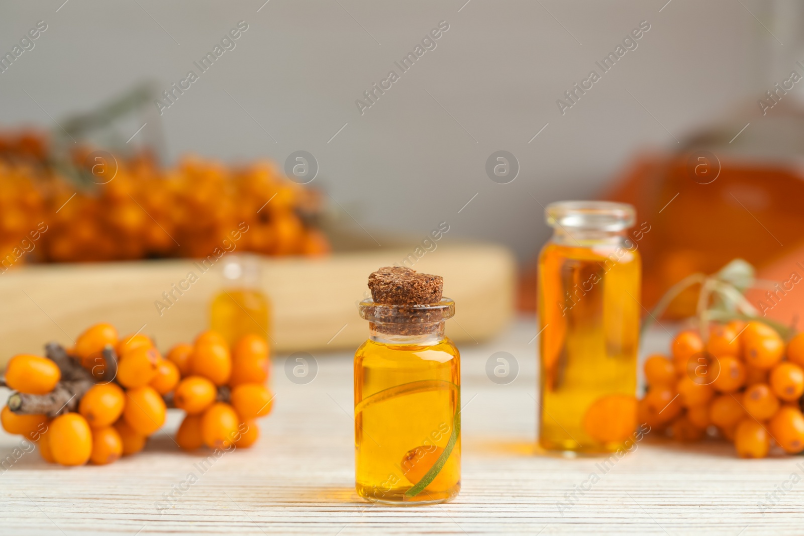 Photo of Natural sea buckthorn oil and fresh berries on white wooden table