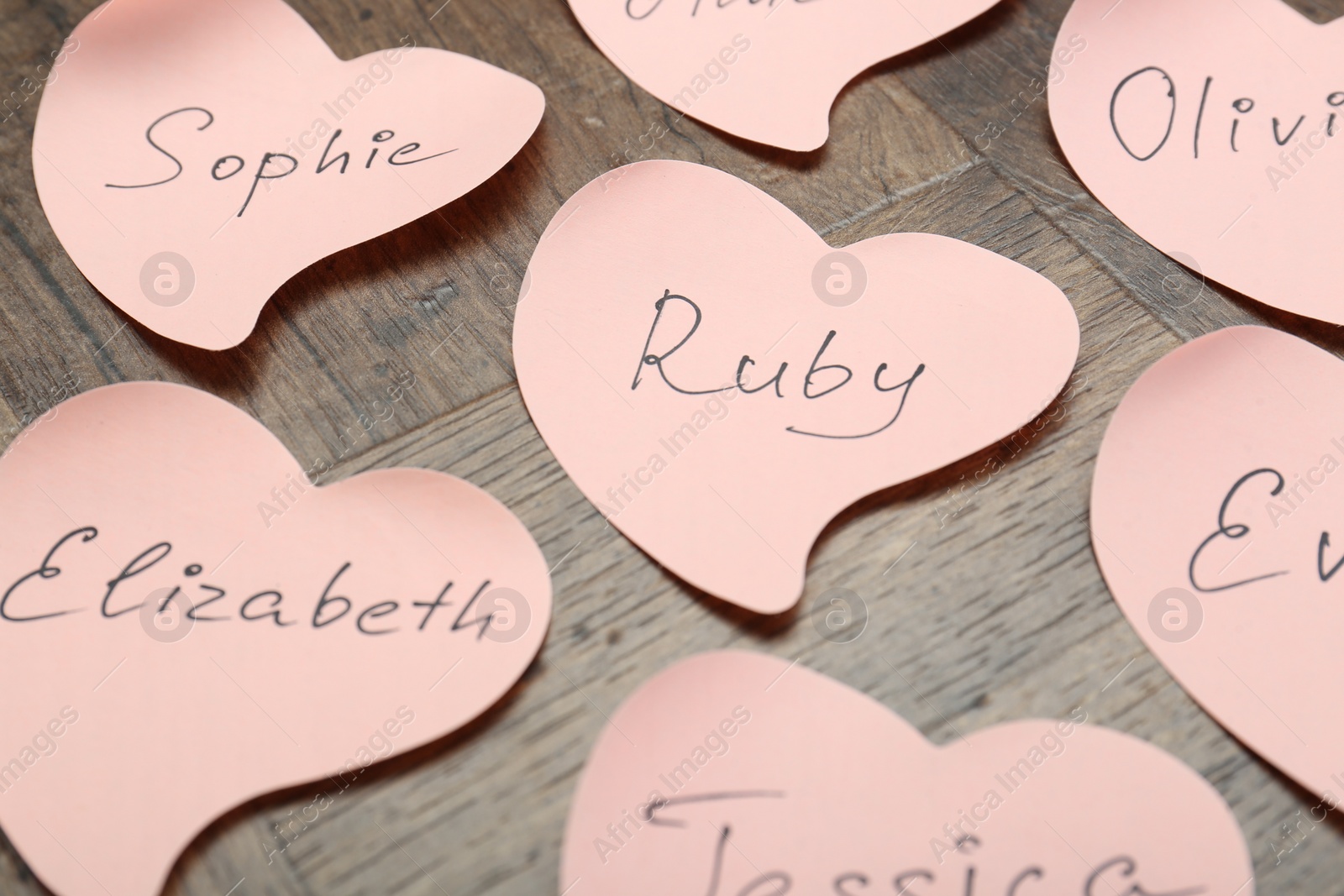 Photo of Paper stickers with different names on wooden table, closeup. Choosing baby's name