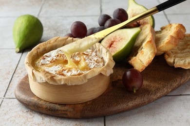 Taking tasty baked brie cheese with knife on light tiled table, closeup