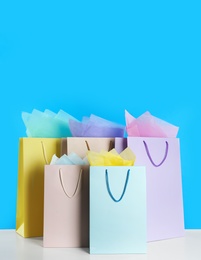 Photo of Colorful gift bags with paper on white table against light blue background