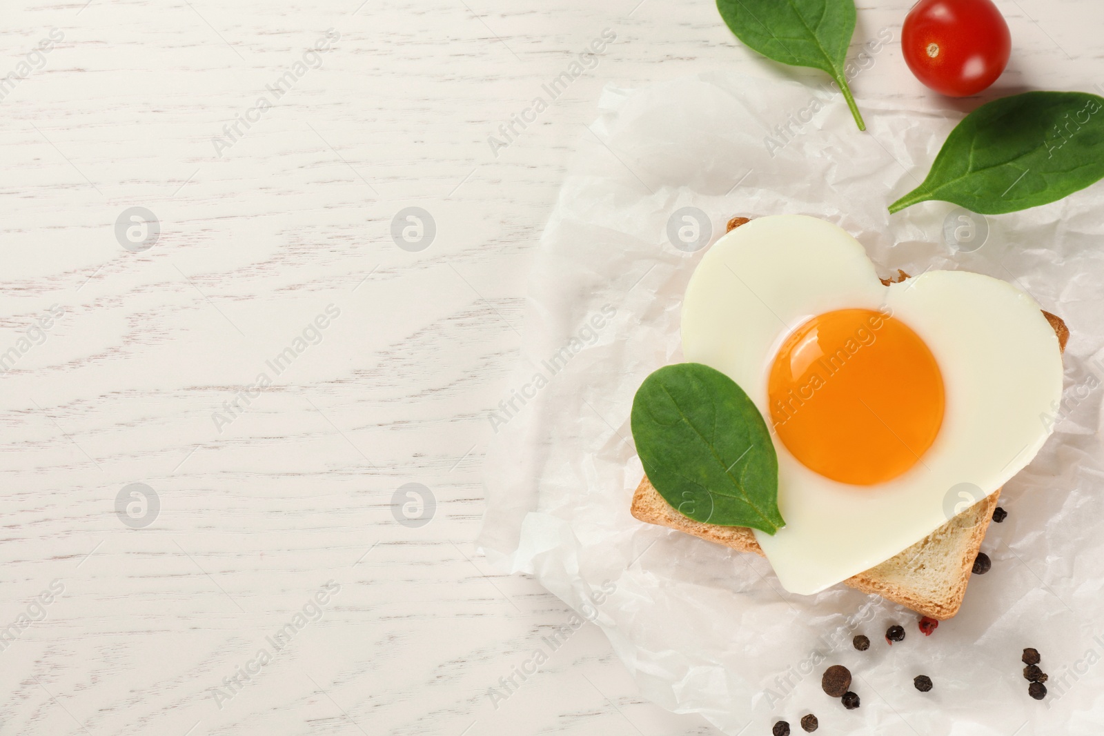 Photo of Heart shaped fried egg with toast, spinach and tomatoes on white wooden table, flat lay. Space for text