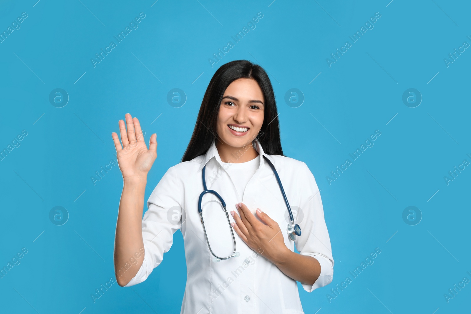 Photo of Happy female doctor waving to say hello on light blue background