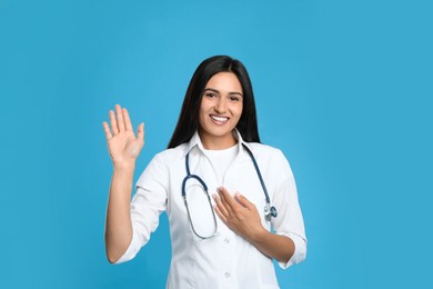 Photo of Happy female doctor waving to say hello on light blue background