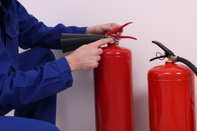 Photo of Man checking quality of fire extinguishers indoors, closeup