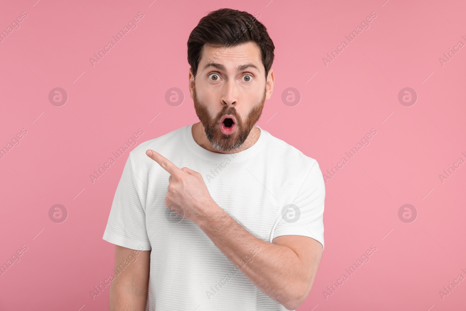 Photo of Surprised man pointing at something on pink background