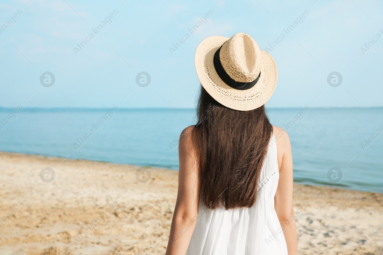 Photo of Beautiful young woman wearing straw hat on beach, back view. Stylish headdress