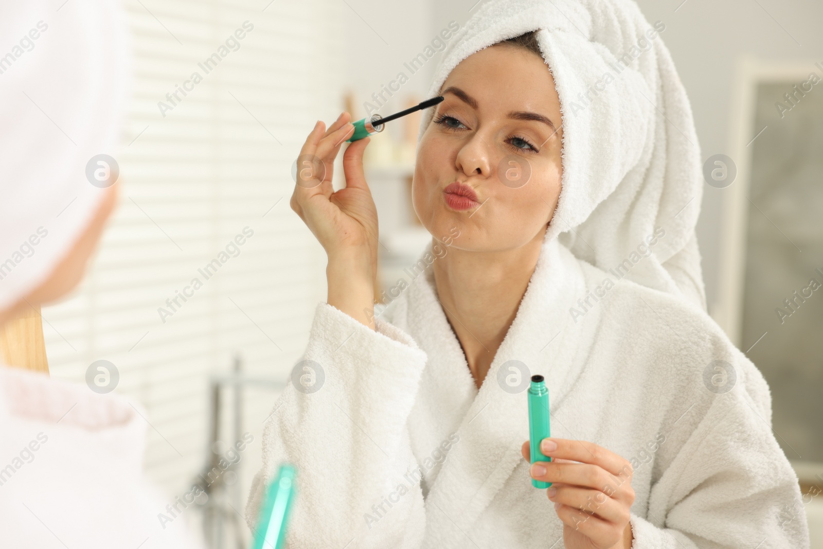 Photo of Beautiful woman applying mascara near mirror in bathroom