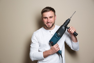 Photo of Young working man with rotary hammer on beige background