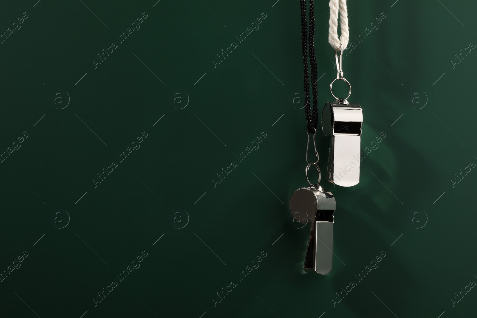 Photo of Referee equipment. Metal whistles on dark green background, closeup and space for text