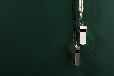 Referee equipment. Metal whistles on dark green background, closeup and space for text