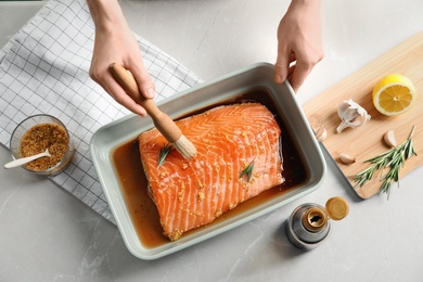 Photo of Woman marinating raw salmon in dish at table