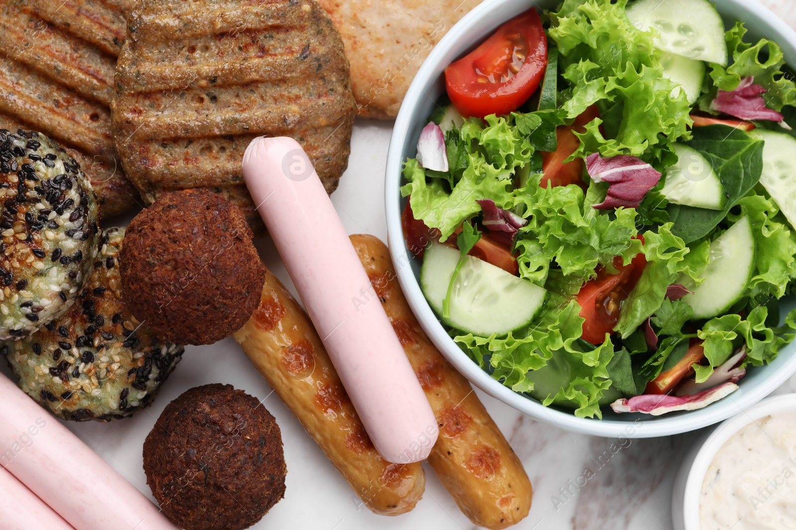 Photo of Different tasty vegan meat products, sauce and fresh vegetable salad on white marble table, flat lay