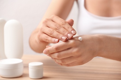 Young woman applying hand cream at table, closeup