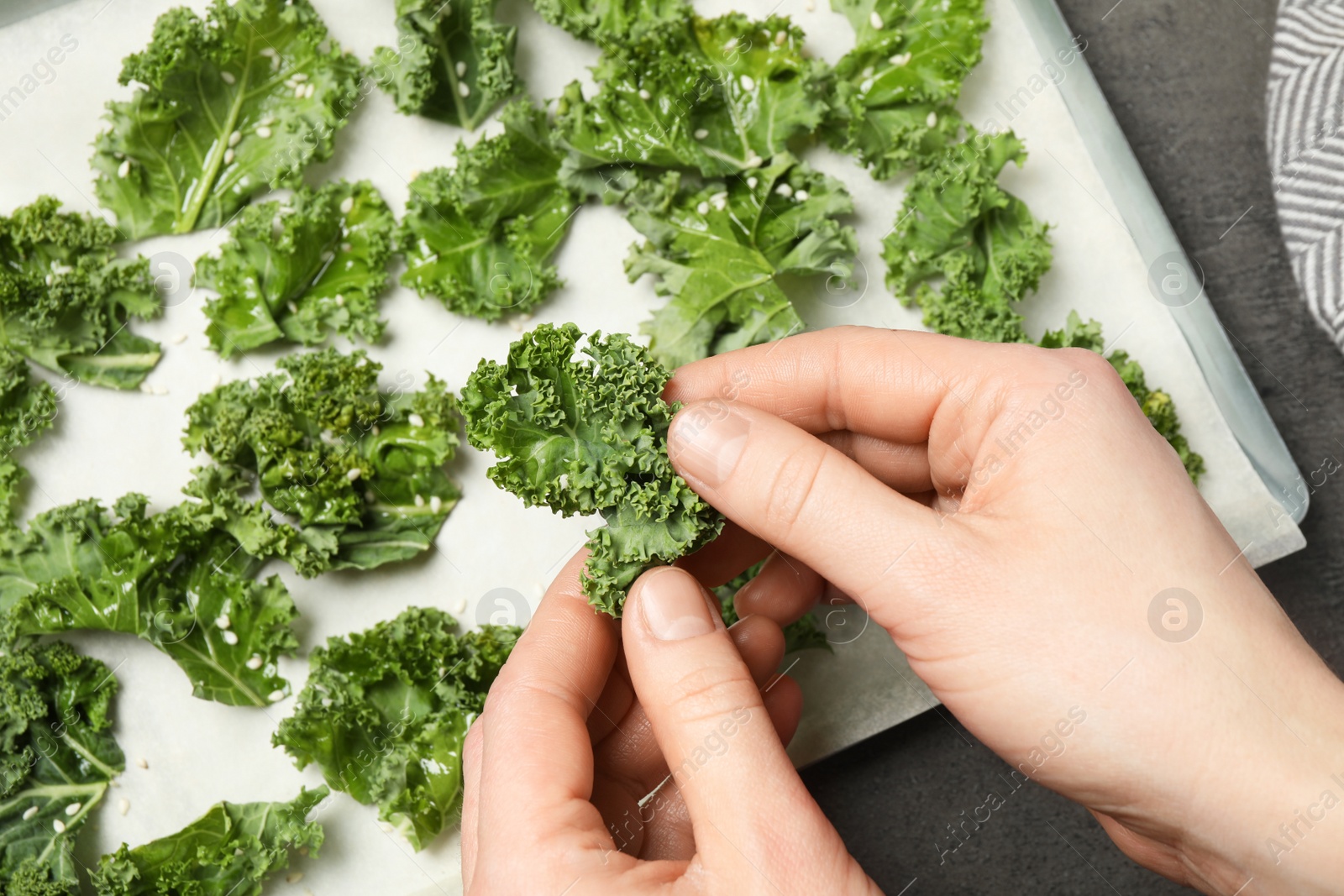 Photo of Woman preparing tasty kale chips at grey table, top view