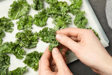 Woman preparing tasty kale chips at grey table, top view