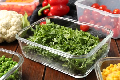 Photo of Containers with arugula and fresh products on wooden table, closeup. Food storage