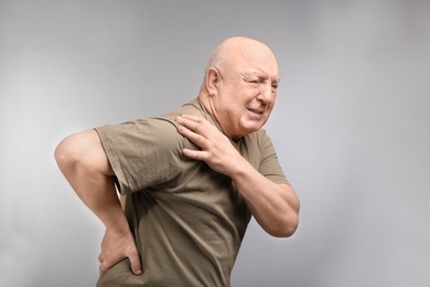 Photo of Senior man suffering from pain in shoulder on light background