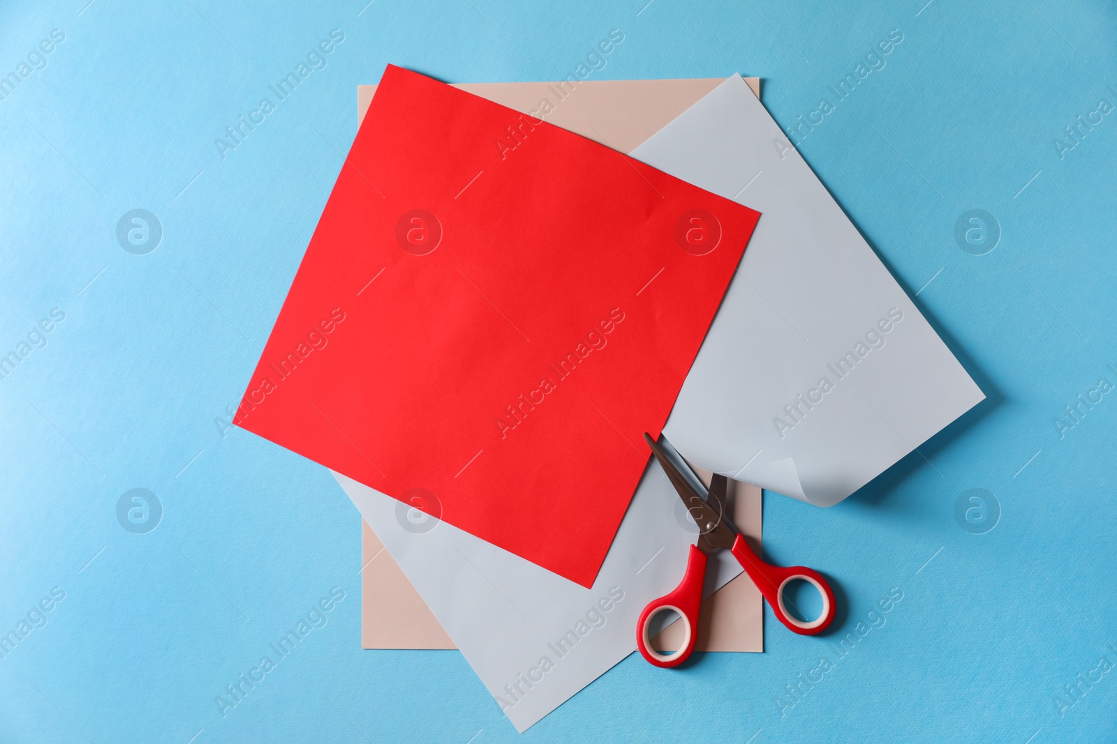 Photo of Red scissors and color sheets of paper on light blue background, flat lay