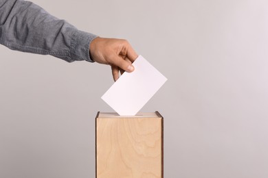 Photo of Man putting his vote into ballot box on light grey background, closeup