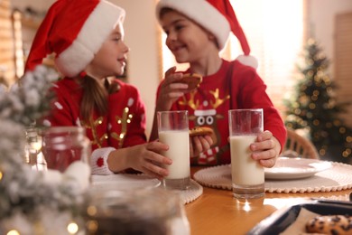 Photo of Cute little children with delicious Christmas cookies and milk at home, focus on hands