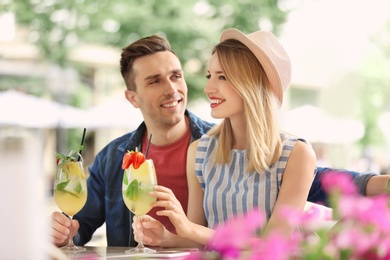 Young couple with glasses of tasty lemonade in open-air cafe