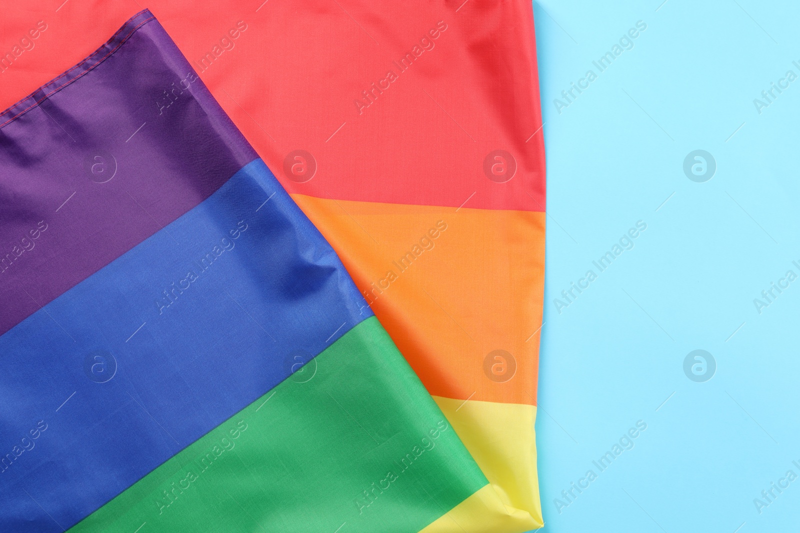 Photo of Rainbow LGBT flag on light blue background, top view