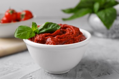 Photo of Tasty tomato paste and basil in bowl on light gray table, closeup