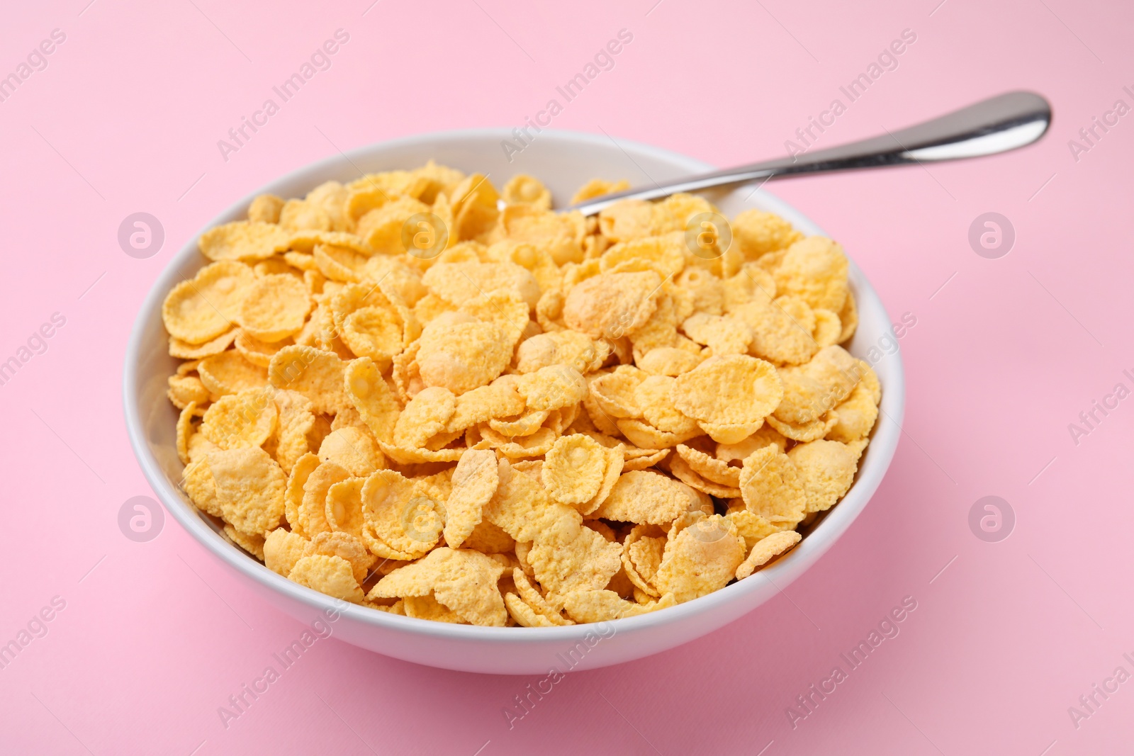 Photo of Breakfast cereal. Tasty corn flakes in bowl and spoon on pink table, closeup