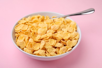 Photo of Breakfast cereal. Tasty corn flakes in bowl and spoon on pink table, closeup