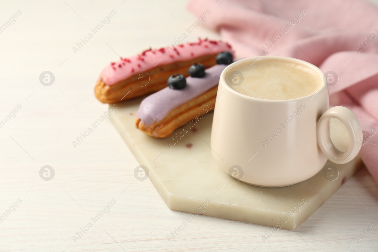 Photo of Cup of coffee and delicious eclairs covered with glaze on white wooden table. Space for text