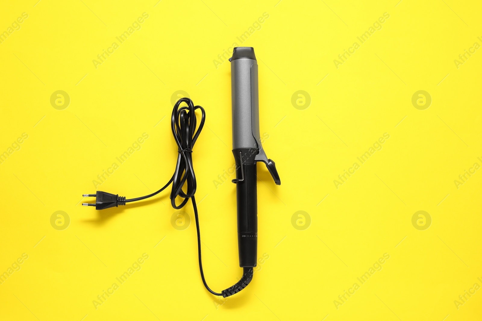 Photo of Curling iron on yellow background, top view