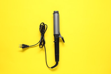 Photo of Curling iron on yellow background, top view