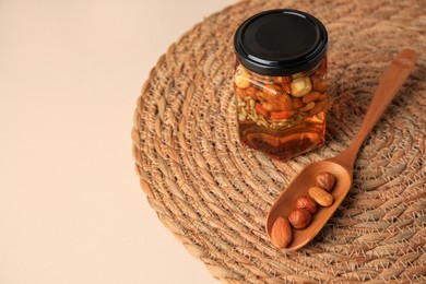Photo of Different nuts with honey in jar and spoon on beige table. Space for text