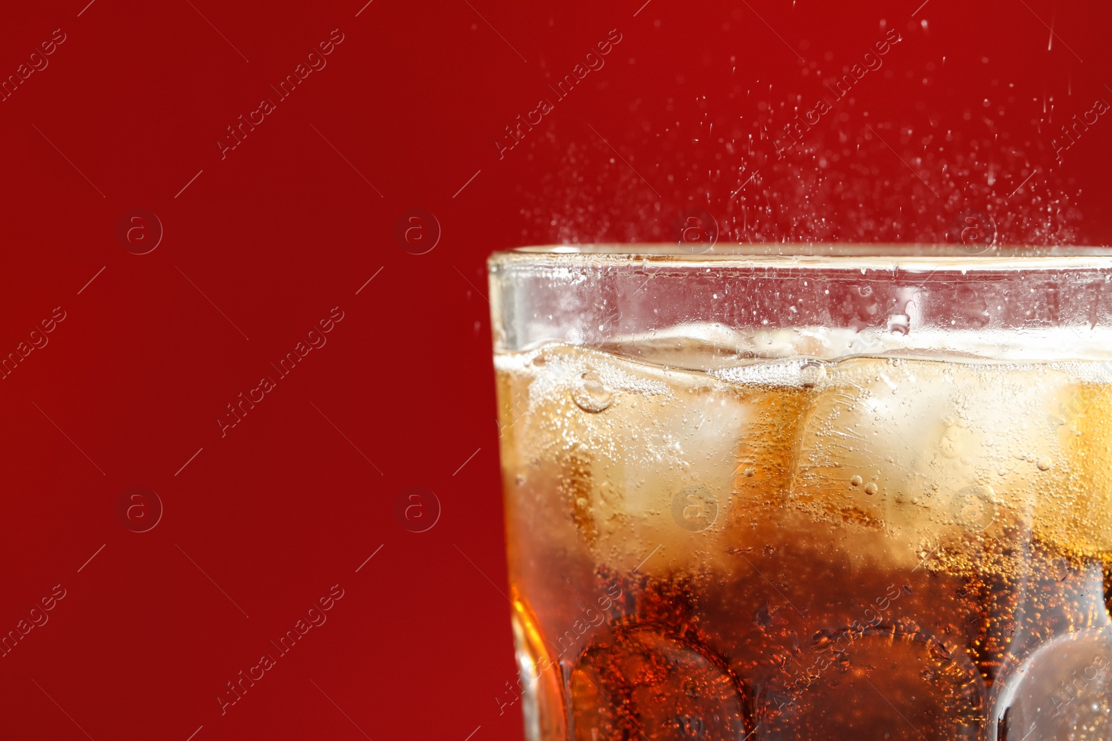 Photo of Glass of refreshing soda drink with ice cubes on red background, closeup. Space for text