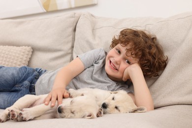 Photo of Little boy hugging cute puppies on couch indoors