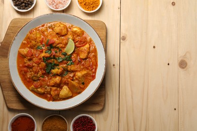 Photo of Delicious chicken curry and spices on wooden table, flat lay. Space for text
